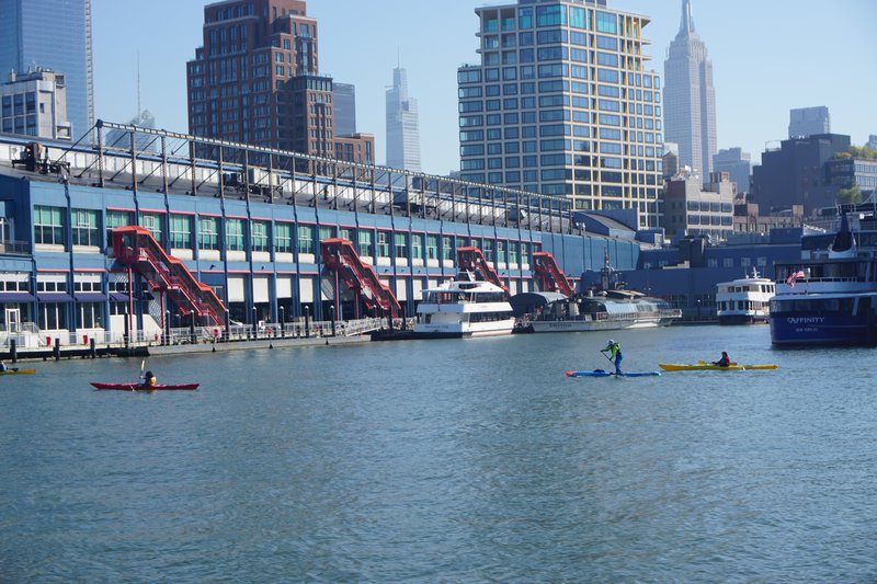 Stand-up paddlers and canoeists on the Hudson River in New York City with the Empire State Building in the background.